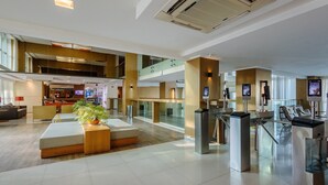A spacious hotel lobby with a modern design, featuring a reception desk, seating area, and a large air conditioning unit.