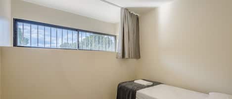 A small, single-bed room with a window, a curtain, and a towel on the bed.