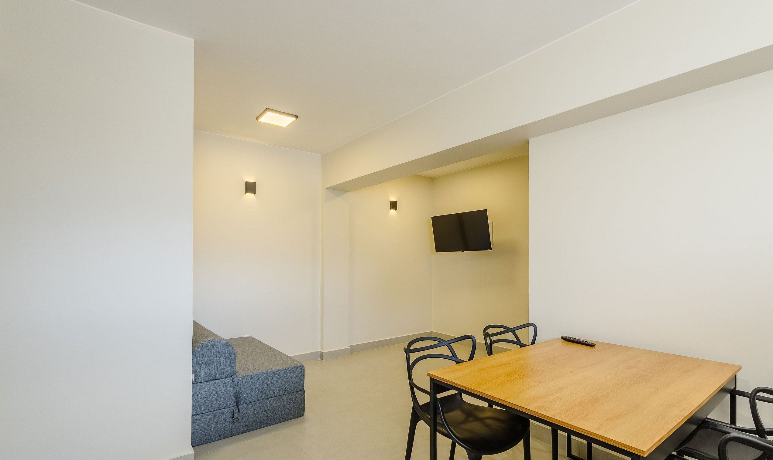 A modern room with a wooden table and chairs, a flat-screen TV mounted on the wall, and a blue sofa.