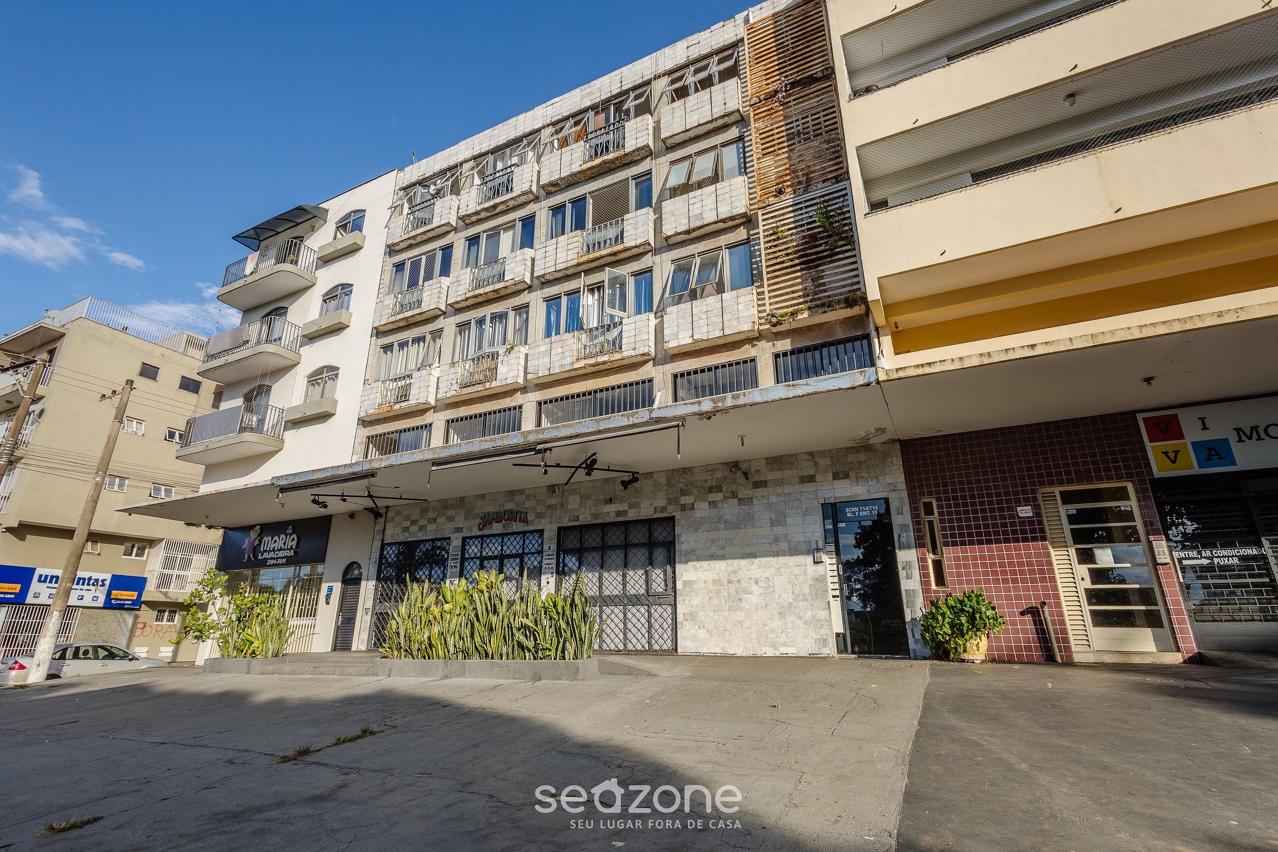 Un edificio a più piani con balconi, un negozio e un'area di parcheggio.