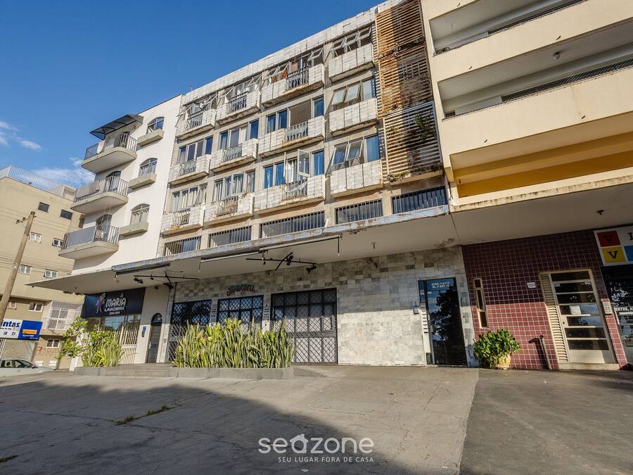 A multi-story building with balconies, a storefront, and a parking area.
