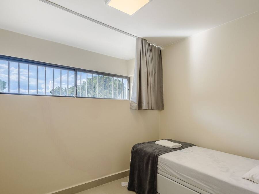 Quarto pequeno com cama de solteiro, janela, cortina e toalha na cama.