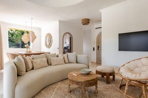 Uma sala de estar moderna com um sofá curvo, uma mesa de centro redonda de madeira e uma poltrona de vime.