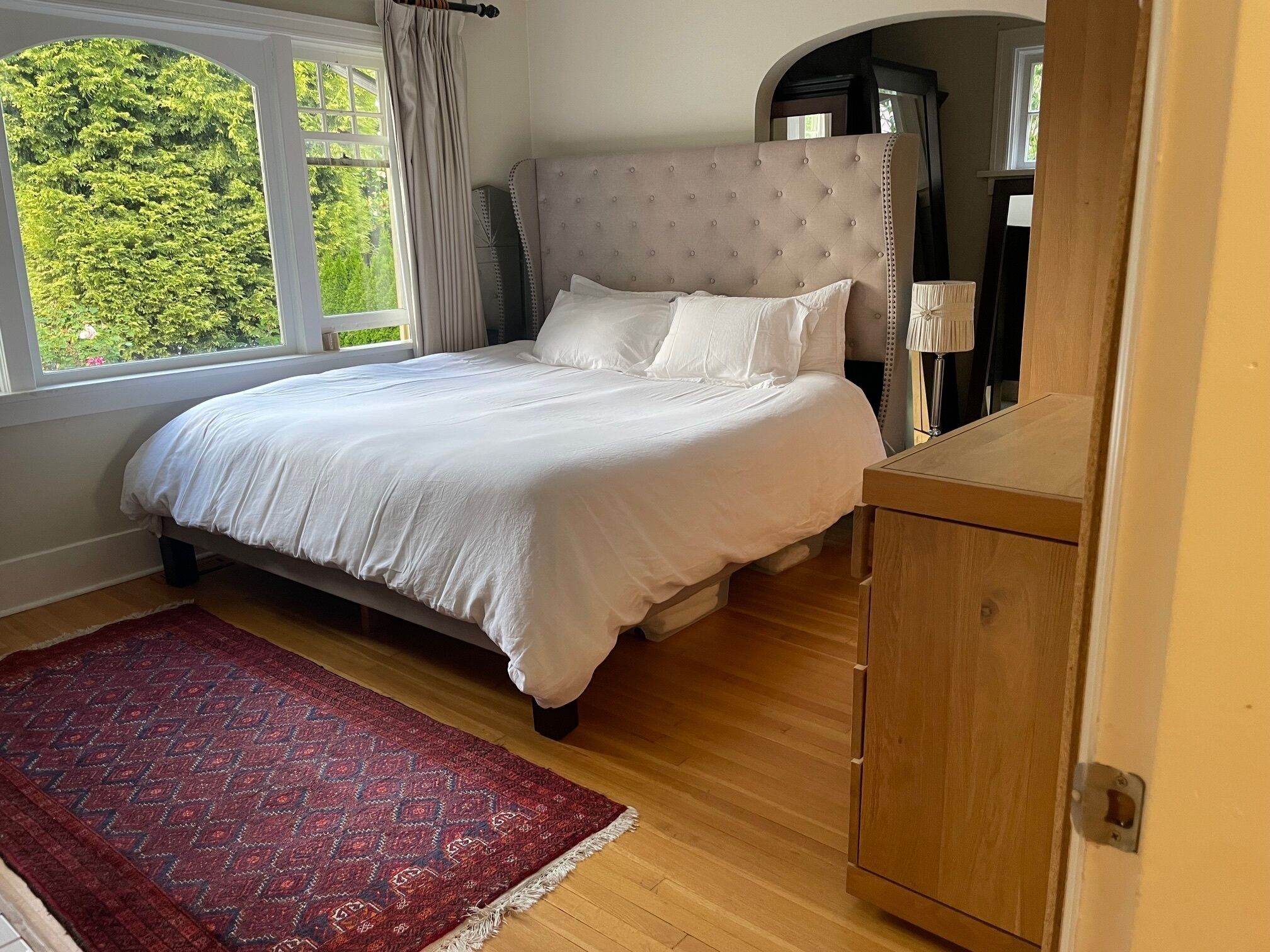 A bedroom with a bed, a red patterned rug, a wooden cabinet, and a window with curtains.