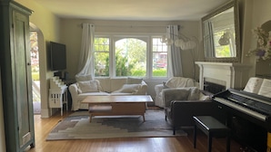 A room with a piano, a sofa, a bench, and a large window with curtains.