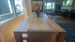 A dining area with a wooden table, chairs, a potted plant, and a colorful abstract wall art.