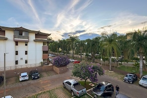 A parking area with multiple cars, a building with balconies, and palm trees. - Apt Facing Lake Paranoa - Clr314 (Brasília)