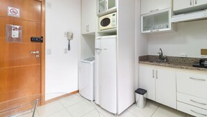 Une cuisine de taille réduite, avec des meubles blancs, un four à micro-ondes, un réfrigérateur et une poubelle.