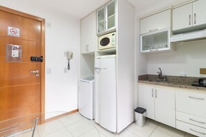 A compact kitchen with white cabinets, a microwave, a refrigerator, and a trash bin.