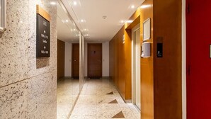 Un couloir d’hôtel avec des panneaux indicateurs, une porte rouge et un appareil fixé au mur.