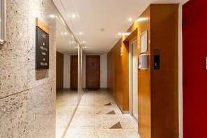 A hotel corridor with directional signs, a red door, and a wall-mounted device.