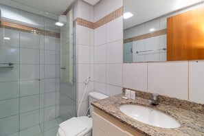 Un baño con cabina de ducha de vidrio, inodoro blanco y lavamanos sobre encimera de granito.