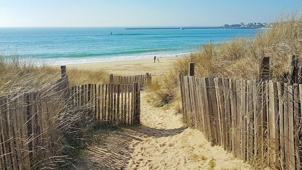 A sandy beach path leading to the ocean, with a wooden fence on one side and a clear view of the sea and distant buildings. - Lovely home in Plouhinec with WiFi (Plouhinec)