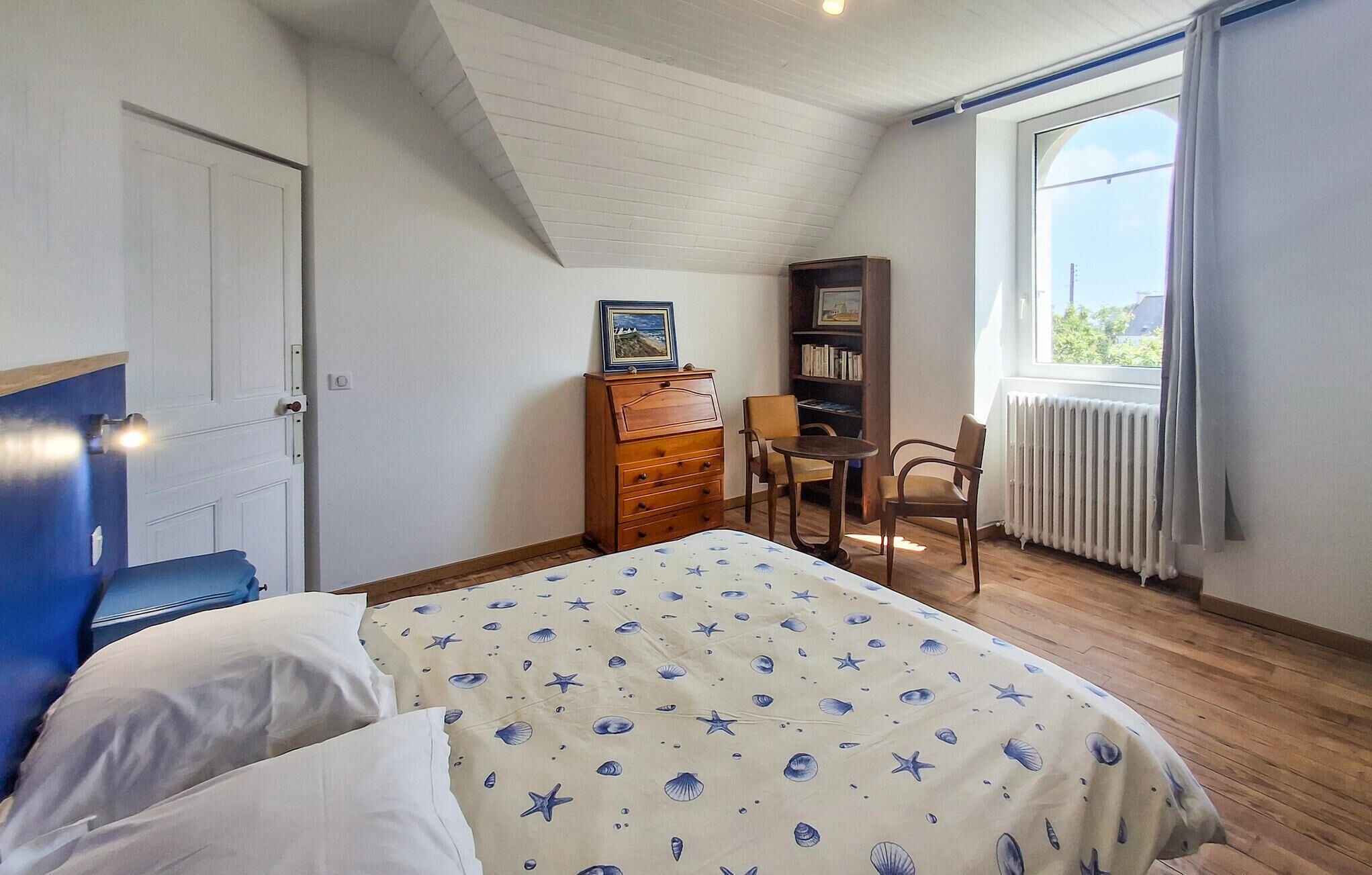 Een slaapkamer met een bed, een houten dressoir, een boekenkast, een stoel en een raam met gordijnen.