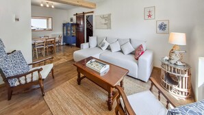 A living room with a white sofa, wooden coffee table, patterned armchair, and a small side table with a lamp. A dining area with a wooden table and chairs is visible in the background. - Lovely home in Plouhinec with WiFi (Plouhinec)