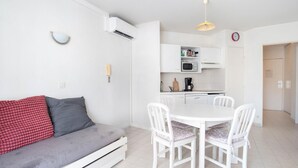 Un espacio habitable moderno y minimalista con un sofá blanco, una mesa de comedor con cuatro sillas, una zona de cocina con armarios blancos y un reloj en la pared.
