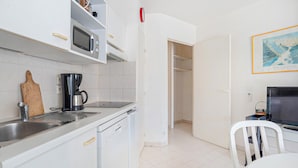 Cocina pequeña equipada con microondas, cafetera y tostadora. Hay una silla blanca y un televisor en la esquina.