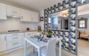 A modern kitchen with white cabinets, a dining table with chairs, and a decorative wall with geometric patterns. - Appartement avec piscine (Saint-Georges-de-Didon)