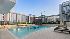 A rooftop swimming pool with lounge chairs and umbrellas, surrounded by modern buildings and construction cranes. - Modern Studio at Paragon (Dubai)