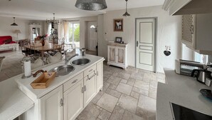 A spacious kitchen with a double sink, white cabinetry, and a large dining area with a red sofa. - Gite avec piscine et jacuzzi (Seigy)