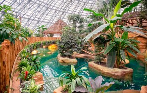 An indoor botanical garden with a glass ceiling, a central water feature, and various tropical plants. - Gite avec piscine et jacuzzi (Seigy)