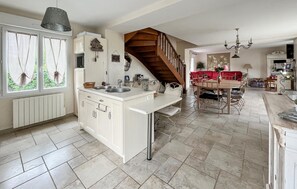 A spacious kitchen with a central island, a dining area with a red sofa, and a staircase leading to another level. - Gite avec piscine et jacuzzi (Seigy)