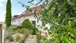 A house with a red-tiled roof, surrounded by a garden with various plants and a tall tree. - Gite avec piscine et jacuzzi (Seigy)