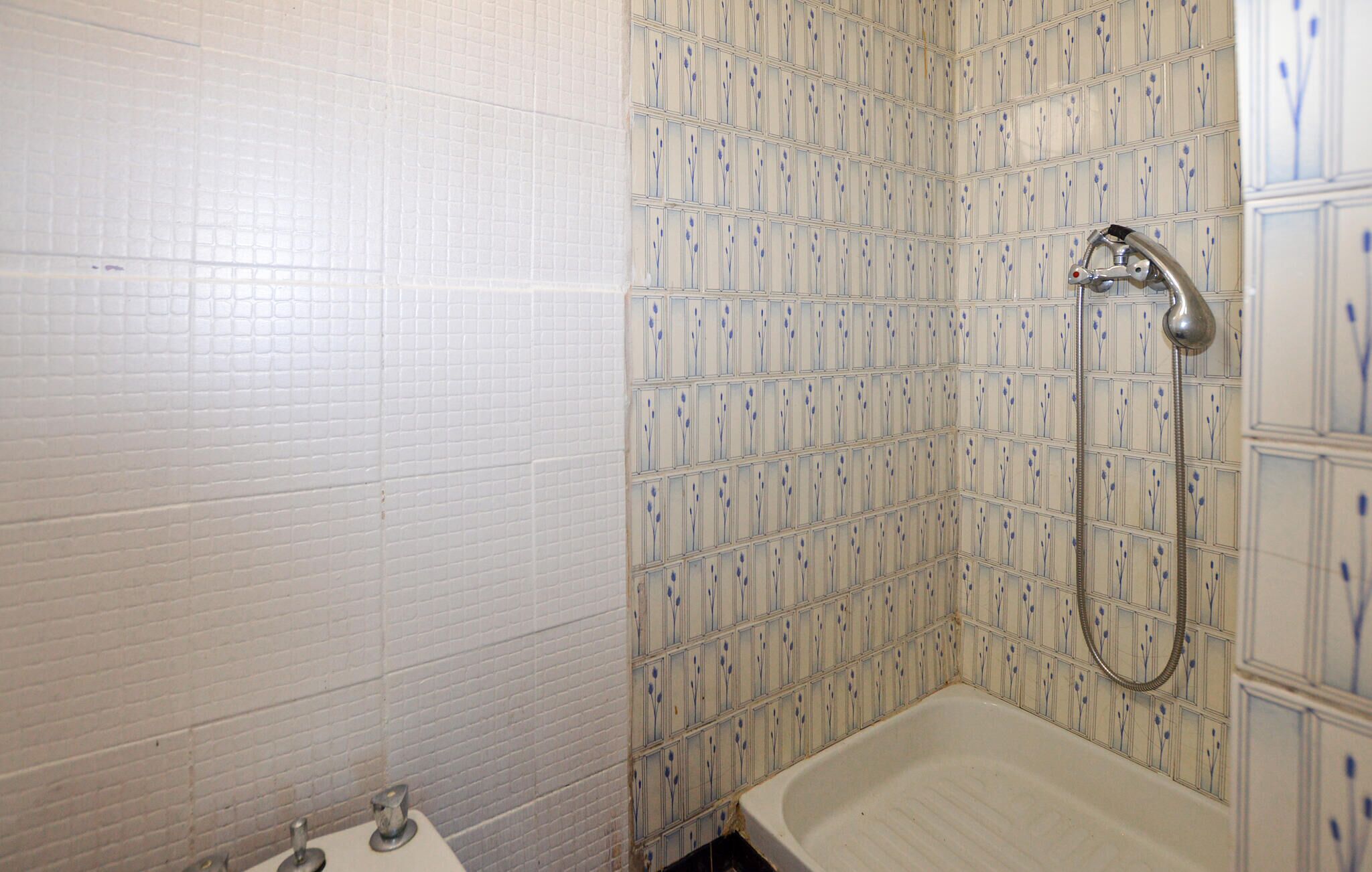 Une salle de bain avec des murs carrelés de carreaux blancs, une douche avec un pommeau de douche amovible et une baignoire.