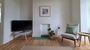 A living room with a flat-screen TV on a stand, a fireplace, a chair, and a small table.