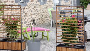 Outdoor seating with a stone wall backdrop, a grill, and potted plants. - Gite Gouville sur Mer (Gouville sur Mer)