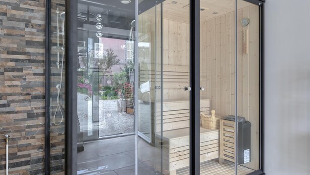 A modern bathroom with a glass door, a shower, and a wooden sauna area. - Gite Gouville sur Mer (Gouville sur Mer)