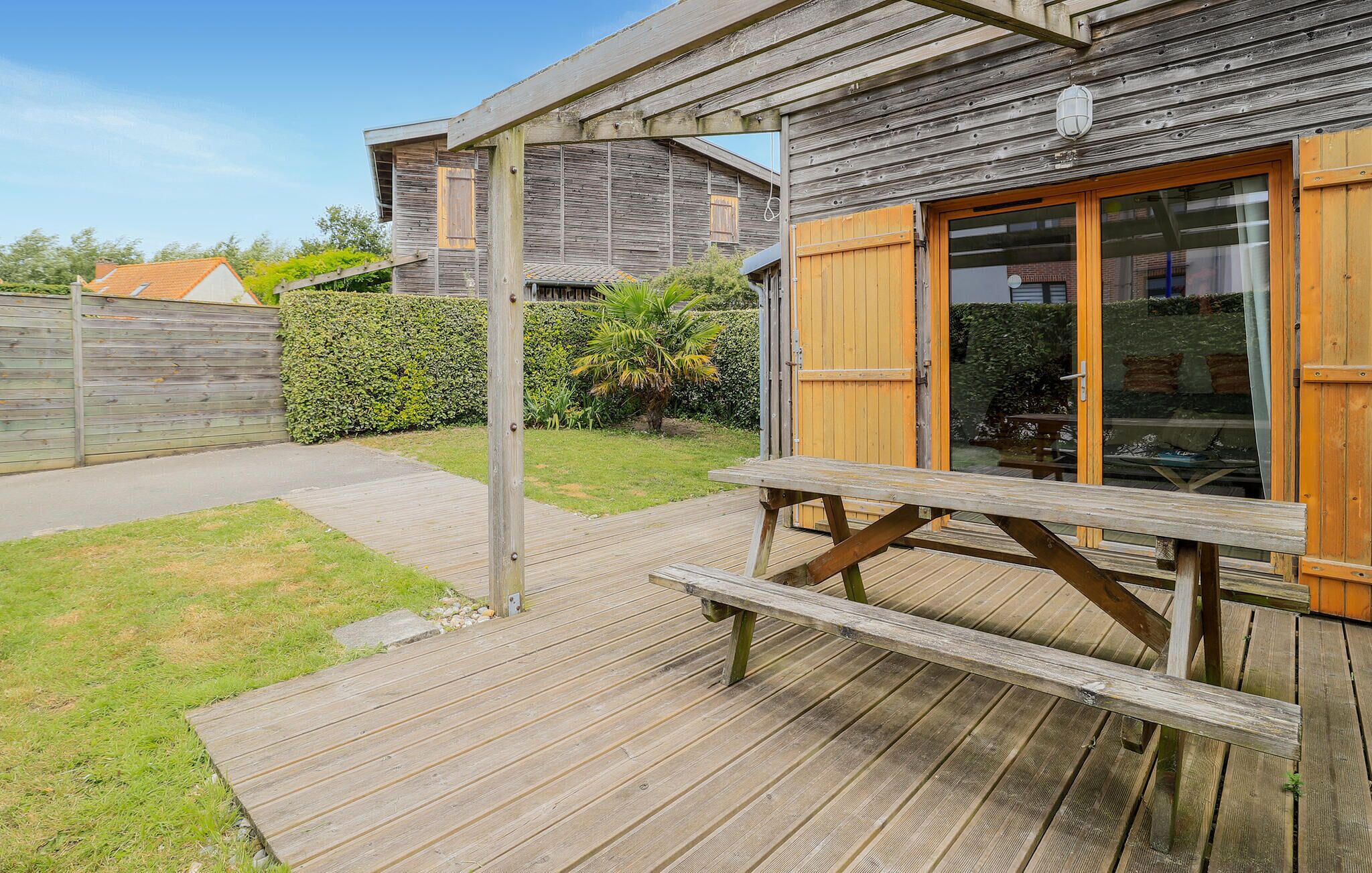 A wooden deck with a picnic table, a wooden fence, and a building with a glass door and wooden shutters.