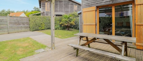 A wooden deck with a picnic table, a wooden fence, and a building with a glass door and wooden shutters.
