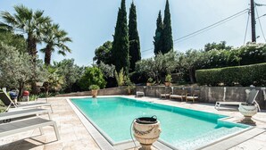 A rectangular swimming pool with a tiled deck, surrounded by palm trees, cypress trees, and various shrubs. - Amazing home in Tourrettes with sauna (Tourrettes)
