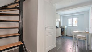 A spacious kitchen with modern appliances, a dining area with a white table and chairs, and a staircase with wooden steps.
