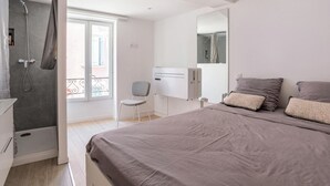 A bedroom with a bed, a chair, a shower, and a window.