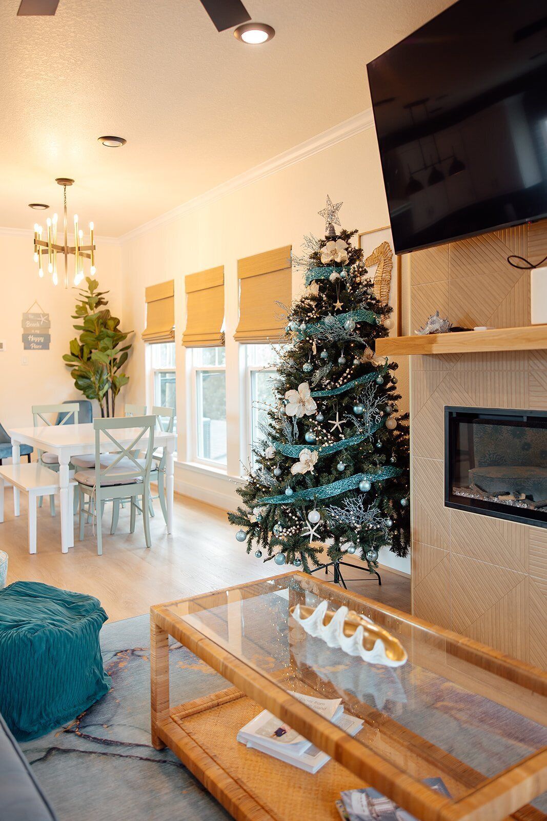 A modern living room with a Christmas tree, a glass coffee table, a fireplace, and a TV mounted on the wall.