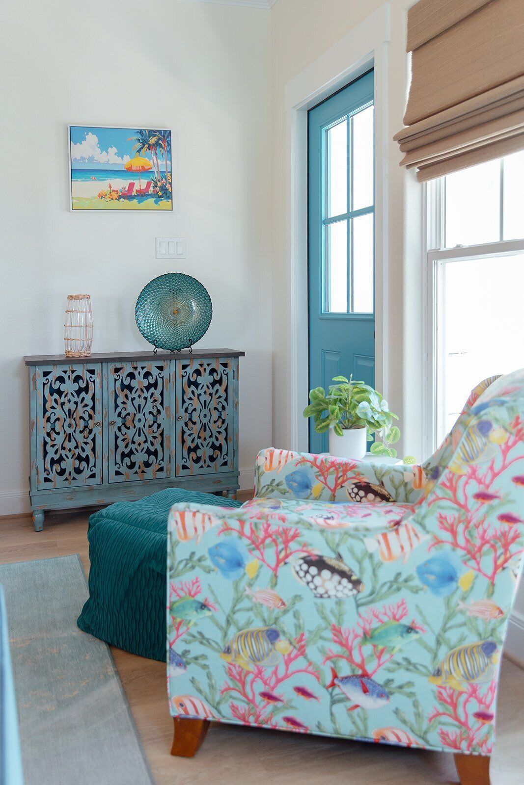 Una habitación con un sofá color turquesa, un aparador decorativo, un cuadro de playa enmarco y una planta en maceta.