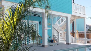 Una casa de dos pisos con piscina, un porche cubierto y una terraza de madera.