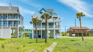 A beachfront property with a two-story house, a covered porch, and a wooden walkway leading to the entrance. - Twin Palms Paradise (Galveston)