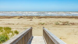 A wooden boardwalk leading to a sandy beach with ocean waves in the background. - Twin Palms Paradise (Galveston)