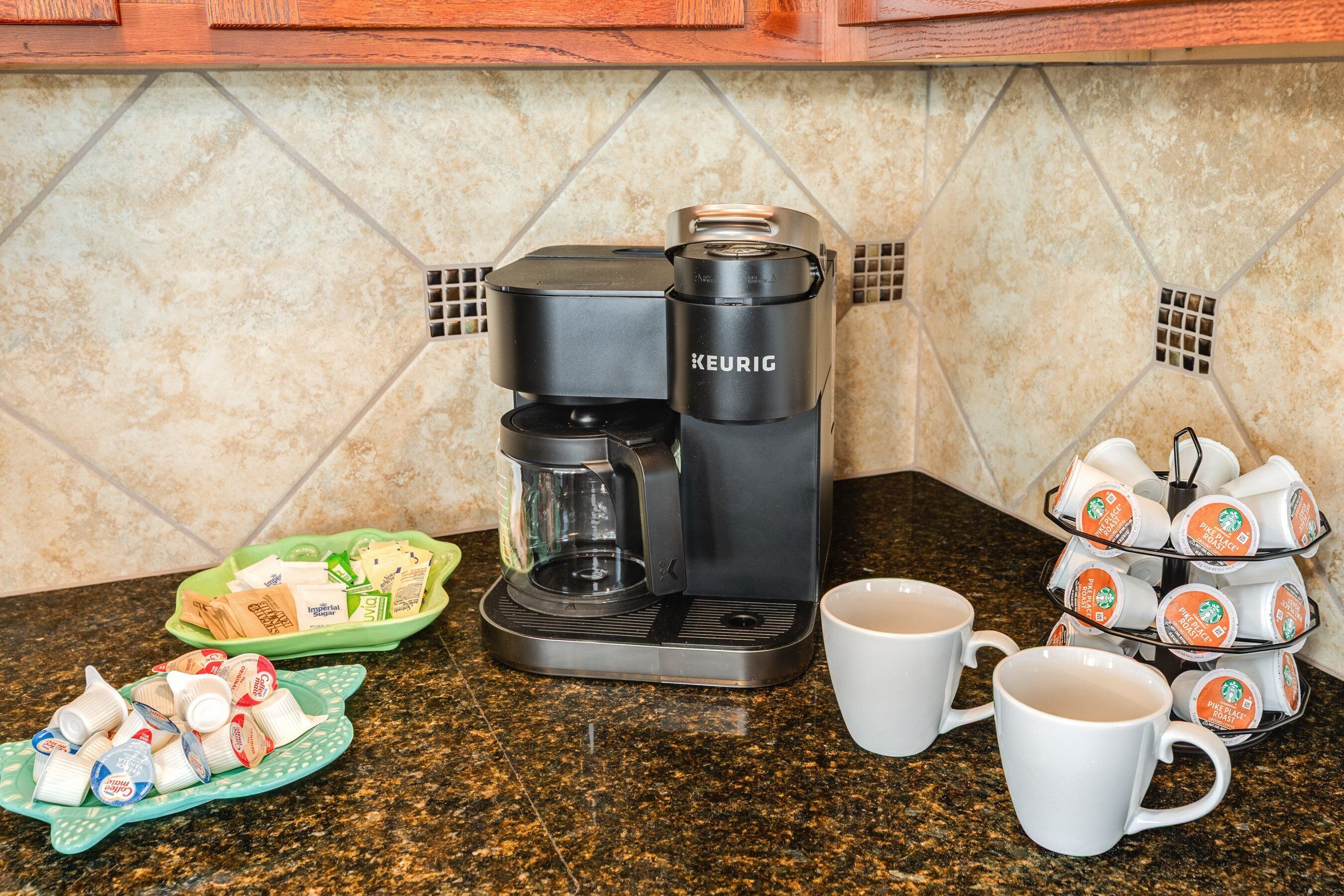 Una cafetera, tazas de café y una bandeja con cápsulas de café sobre una encimera de cocina.
