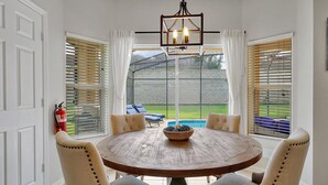 A dining area with a round wooden table and four upholstered chairs, a hanging light fixture, and large windows with blinds. - 3 Miles to Disney! Free Heated Saltwater Pool & Spa, Star Wars Game Room, BBQ! (Kissimmee)