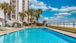 A swimming pool with clear blue water, surrounded by palm trees and a building with balconies.