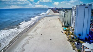 A beachside hotel with a long beachfront, a parking lot, and a pool area.