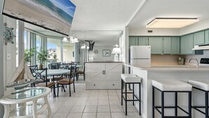 A modern kitchen with a central island, bar stools, and a dining area with a round table and chairs. - Santa Rosa Dunes 912 | Olympic Size Pool & More | My Beach Getaways (Pensacola Beach)