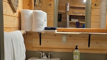 A wooden cabin bathroom with a sink, toilet, and three pendant lights.