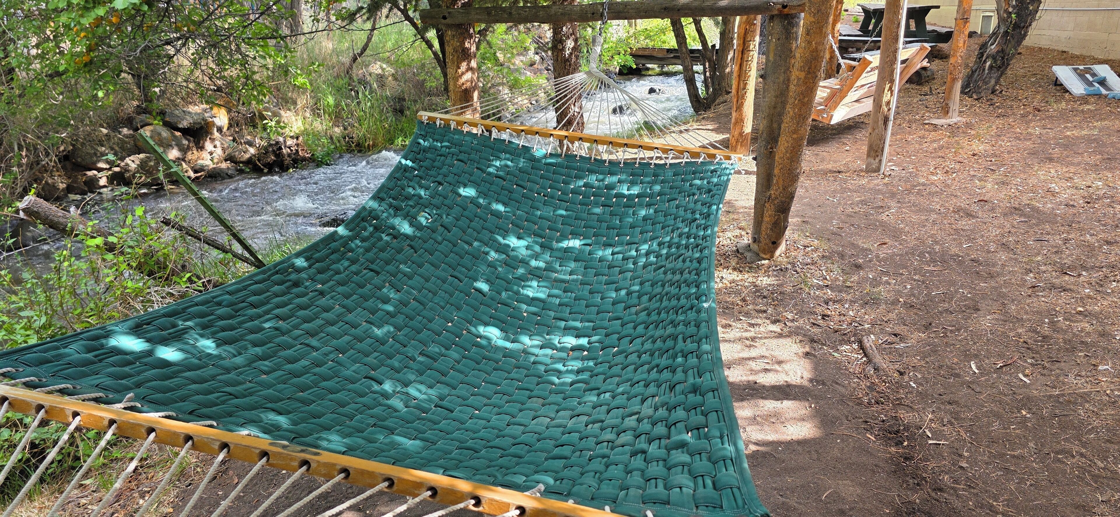 A hammock in a natural setting with a dirt ground and trees in the background.