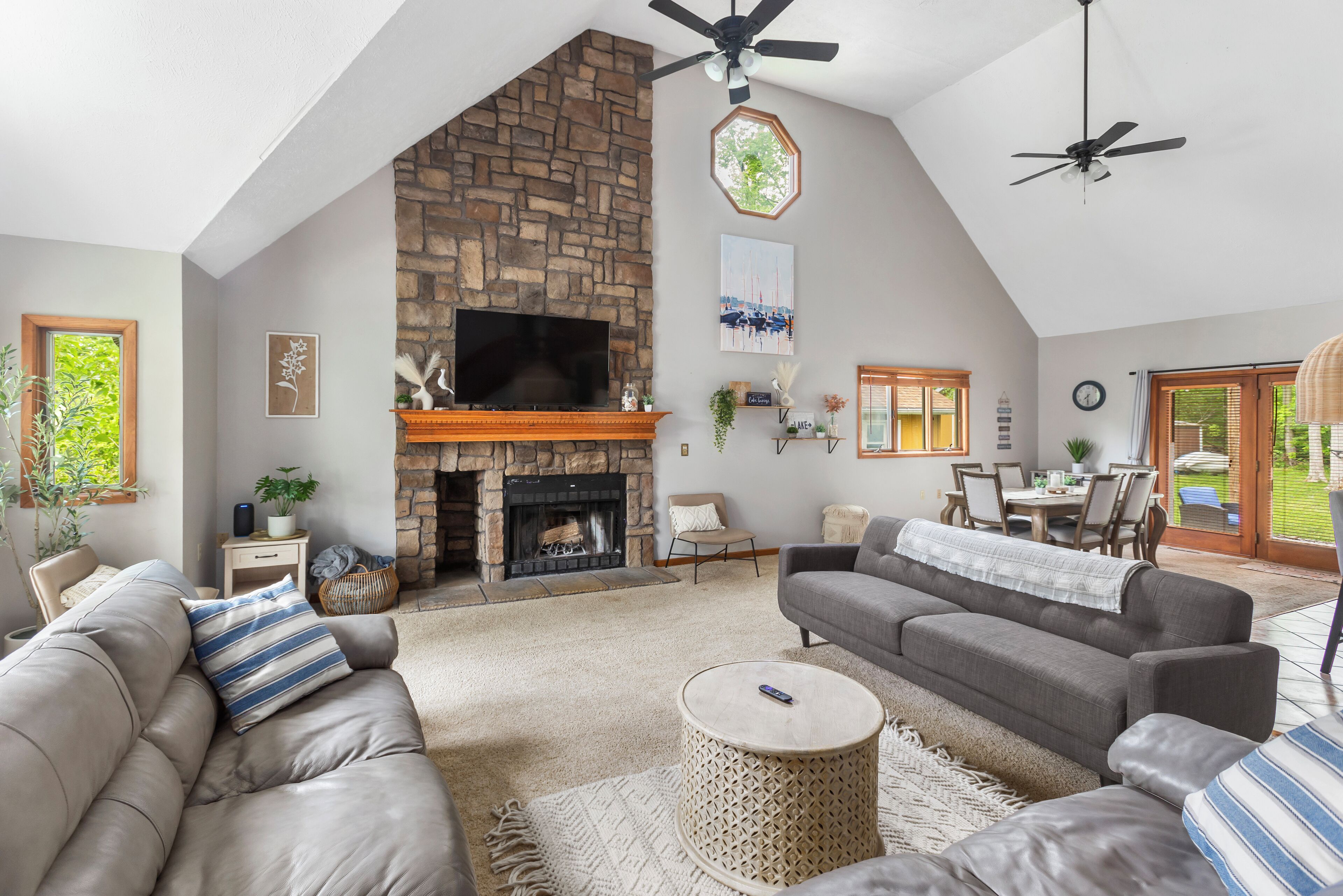 A spacious living room with a stone fireplace, two sofas, a TV, and a ceiling fan.