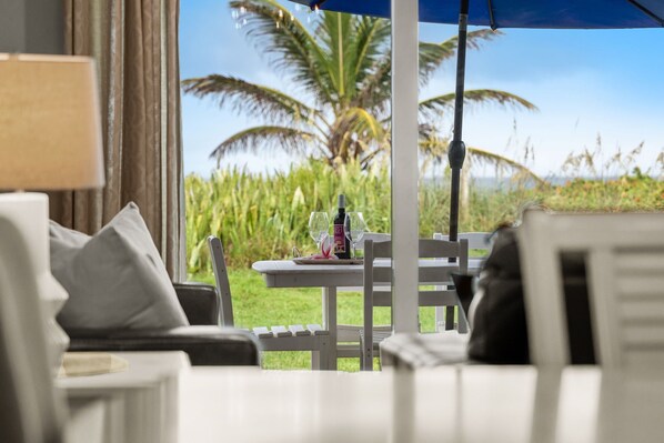 A seating area with a table set for two, a bottle of wine, and a view of palm trees and greenery.